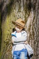 menino bonito posando com um chapéu de cowboy na floresta por uma árvore. os raios do sol envolvem o espaço. história de interação para o livro. espaço para copiar foto