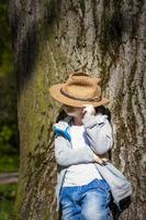menino bonito posando com um chapéu de cowboy na floresta por uma árvore. os raios do sol envolvem o espaço. história de interação para o livro. espaço para copiar foto
