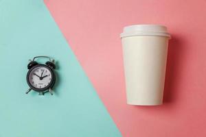 xícara de café de papel de design simplesmente plana e despertador em fundo moderno colorido pastel rosa azul. bebida para viagem e bebida de pequeno-almoço. bom dia acorde acordado conceito. espaço de cópia da vista superior.