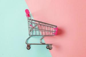 carrinho de supermercado pequeno supermercado para brinquedo de compras com rodas isoladas em papel colorido pastel azul e rosa na moda espaço de cópia de fundo geométrico. venda comprar conceito de consumidor de loja de mercado de shopping. foto