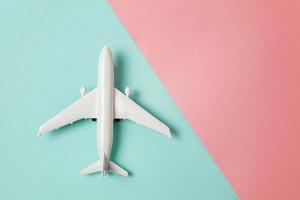 avião de modelo de brinquedo em miniatura de design simplesmente plano leigo em fundo geométrico moderno de papel colorido pastel azul e rosa. viajar de avião férias verão fim de semana mar aventura viagem conceito. foto