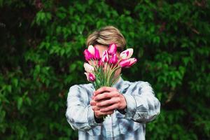 cara segura um buquê de tulipas segurando-os na frente dele foto