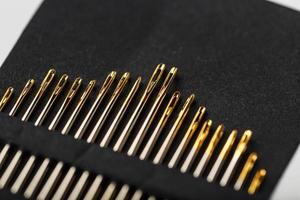 agulhas de costura de ouro em um fundo preto em uma fileira. foto