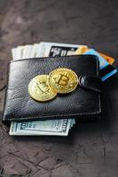 uma carteira preta com dólares, e-cards e bitcoins em um plano de fundo texturizado preto. foto