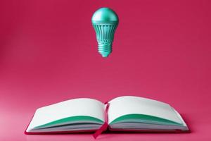 a lâmpada paira sobre as páginas abertas de um caderno vazio em um fundo rosa. foto