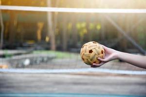 bola sepak takraw, esporte tradicional dos países do sudeste asiático, segurando na mão do jovem jogador sepak takraw feminino asiático na frente da rede antes de jogá-lo para outro jogador para chutar a rede. foto