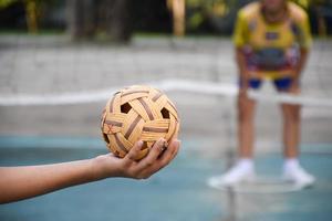 bola sepak takraw, esporte tradicional dos países do sudeste asiático, segurando na mão do jovem jogador sepak takraw feminino asiático na frente da rede antes de jogá-lo para outro jogador para chutar a rede. foto