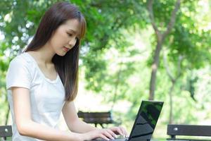 mulher asiática sentada com um laptop em um parque foto