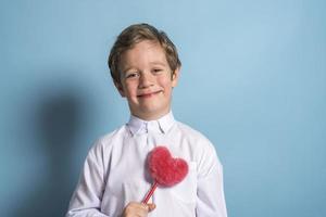 um menino europeu em uma camisa branca tem um coração vermelho fofo nas mãos foto