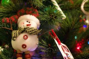 boneco de neve de feltro em uma árvore de abeto com decorações de natal e luzes desfocadas. foto