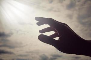 mão estendendo a mão para a luz brilhante no céu acima. conceito religioso e espiritual foto