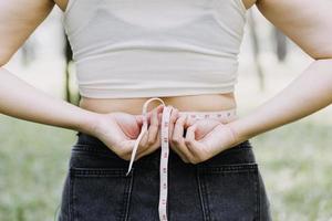 linda mulher gorda com fita métrica ela usa a mão para espremer o excesso de gordura que está isolado em um fundo branco. ela quer perder peso, o conceito de cirurgia e quebrar a gordura sob o foto