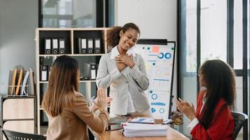 Mulher de negócios asiática de meia idade, gerente executiva, mostrando aos colegas os números de dados de receita da equipe planejando na tela grande no escritório foto