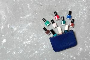 bolsa cosmética de mulher com manicure e pedicure, vernizes de gel brilhantes sobre fundo cinza de cimento com espaço de cópia para seu projeto e texto. conceito de postura plana de trabalho de unhas foto