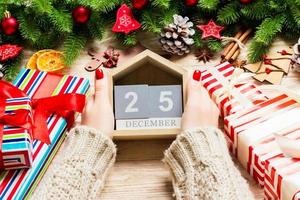 vista superior das mãos femininas segurando um calendário em fundo de madeira. dia vinte e cinco de dezembro. decorações de férias. conceito de natal foto