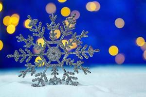 grande floco de neve brilhante na neve e fundo azul com bokeh amarelo feliz natal e cartão de ano novo. espaço de cópia foto