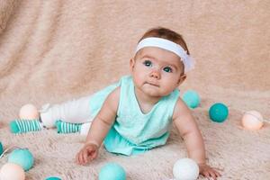 menina bonitinha com lindos olhos azuis em vestido azul está sentado em uma manta de pelúcia bege com luzes de natal antes da véspera de natal. foto