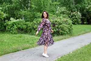 mulher jovem e bonita no vestido preto-roxo está andando em um jardim com arbustos lilás florescendo. foto