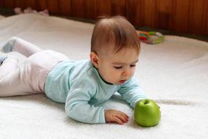 menina está deitada em uma manta branca na sala de estar e brincando com maçã verde. foto