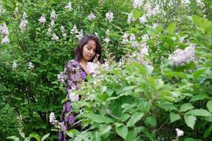 retrato de mulher jovem e bonita no vestido preto-roxo em um jardim com arbustos lilás florescendo. foto