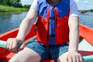 um homem em um barco vermelho, shorts e colete salva-vidas está remando com remos em um barco para passear na água do mar do rio lago na natureza foto