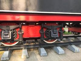 grandes rodas de ferro de um trem vermelho e preto sobre trilhos e elementos de suspensão com molas de uma antiga locomotiva a vapor industrial foto