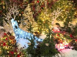 Decoração de Natal. decoração fofa para vitrine. veado feito de guirlandas luminosas. cervo artesanal brilhante e bonito. ao lado de árvores de natal artificiais decoradas com bolas foto