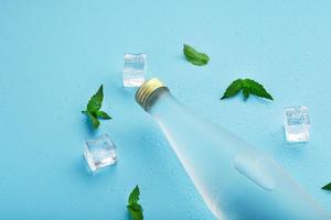 garrafa com uma bebida gelada, cubos de gelo, gotas e folhas de hortelã em um fundo azul. foto