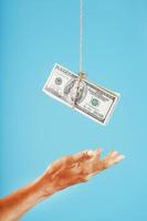 a palma estende a mão para o dinheiro suspenso em uma corda, em um fundo azul. foto