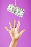 uma mão tenta pegar o dinheiro em uma corda em um fundo rosa. foto