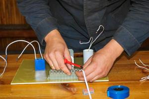 um homem que trabalha eletricista trabalha, coleta o circuito elétrico de uma grande lâmpada de rua branca com fios, um relé em uma fábrica de planta industrial foto