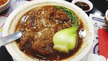 carne estufada de hong kong com espinafre verde na tigela branca e molho agridoce no restaurante tailandês. carne cozida, comida asiática e quente foto