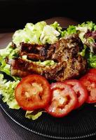 feche o bife de costelas grelhadas com tomate fresco fatiado, repolho verde e espinafre em prato preto ou prato. churrasco de carne de porco com legumes. foto