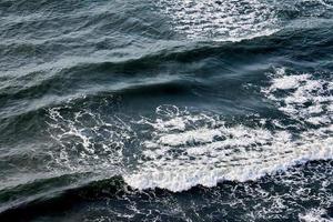 águas do mar azul profundo espirrando com ondas espumosas, superfície da água ondulada azul escuro do oceano, spray do mar foto