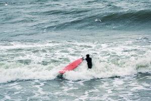 surfista masculino em traje de banho nas ondas do mar com prancha vermelha foto