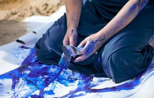 artista performática feminina em vestido azul escuro manchado com pintura guache azul com traços largos na tela foto