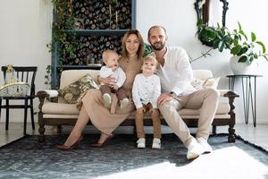 família tradicional mãe pai dois meninos filhos com sorrisos olhando para a câmera sentada no sofá foto