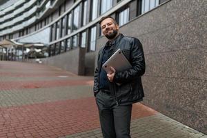 retrato de um empresário adulto do sexo masculino com um laptop ao lado de um prédio administrativo na cidade foto