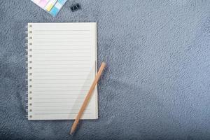 imagem de vista superior do notebook com lápis, mini nota de papel colorida e clipe de papel no tapete cinza foto