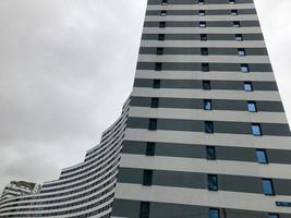 edifício residencial alto, arranha-céu em forma de onda. do lado, a casa é azul e branca. muitas pequenas janelas de vidro ao redor do perímetro. arranha-céu no fundo do céu nublado foto