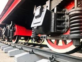 grandes rodas de ferro de um trem vermelho e preto sobre trilhos e elementos de suspensão com molas de uma antiga locomotiva a vapor industrial foto