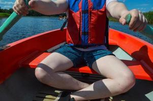 um homem em um barco vermelho, shorts e colete salva-vidas está remando com remos em um barco para passear na água do mar do rio lago na natureza foto