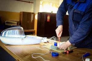 um homem que trabalha eletricista trabalha, coleta o circuito elétrico de uma grande lâmpada de rua branca com fios, um relé em uma fábrica de planta industrial foto