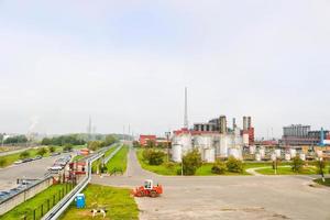 paisagem industrial com plantas químicas, tubos e colunas. abaixo está um trator laranja. fumaça vem do reator. vista panorâmica da produção de reparos. tubos de processo foto