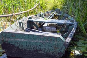 velho barco quebrado em ruínas de madeira para nadar nas margens do rio, lago, mar na grama e juncos na natureza foto