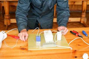 um homem que trabalha eletricista trabalha, coleta o circuito elétrico de uma grande lâmpada de rua branca com fios, um relé em uma fábrica de planta industrial foto