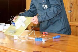 um homem que trabalha eletricista trabalha, coleta o circuito elétrico de uma grande lâmpada de rua branca com fios, um relé em uma fábrica de planta industrial foto