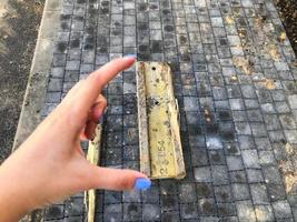 pedaço de metal amarelo e enferrujado metálico encontra-se no asfalto. garota com manicure azul segura metal com os dedos. seção perigosa da estrada em um canteiro de obras foto