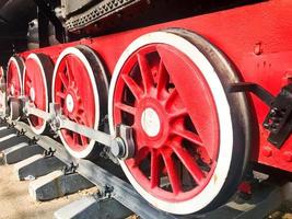 grandes rodas de ferro de um trem vermelho e preto sobre trilhos e elementos de suspensão com molas de uma antiga locomotiva a vapor industrial foto