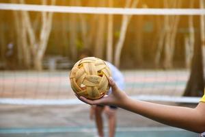 bola sepak takraw, esporte tradicional dos países do sudeste asiático, segurando na mão do jovem jogador sepak takraw feminino asiático na frente da rede antes de jogá-lo para outro jogador para chutar a rede. foto